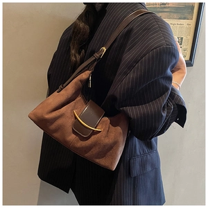 Détail d'un sac sous les bras en daim marron avec boucle dorée sur un blazer rayé