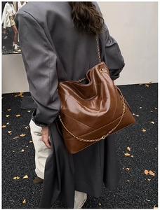 Detail of a brown quilted leather tote bag with gold chain strap in an urban fashion setting