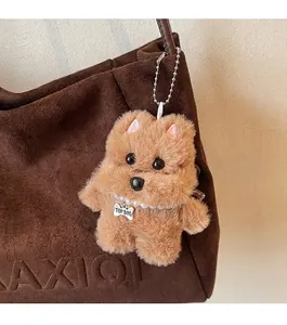 Nahaufnahme eines braunen Plüschhund-Anhängers mit Perlenkette an einer Wildleder-Einkaufstasche