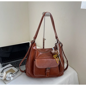 Close-up of a retro reddish-brown leather hobo bag with buckled pocket and bear pendant