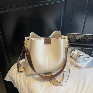 Détail du sac seau crème avec écusson logo marron et large bandoulière rayée