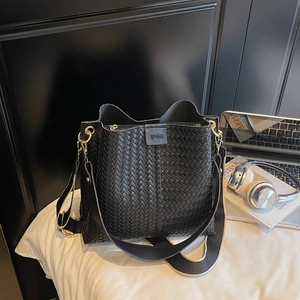Détail du sac seau noir tissé avec ferrures dorées et bandoulière en toile