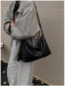 Detail of black leather hobo bag with braided strap and chain on autumn street background