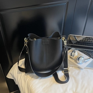Détail du sac seau en cuir noir mat avec large bandoulière tissée et finitions dorées