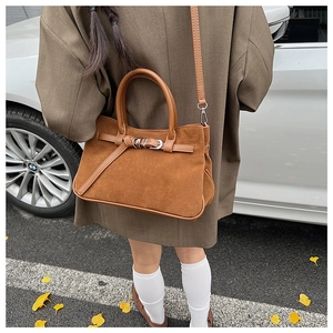 Brown suede baguette bag with buckle strap detail shown in a stylish outdoor setting