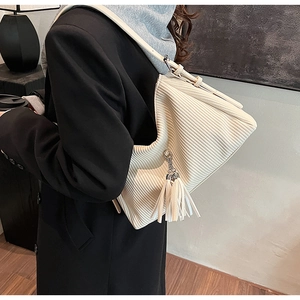 Nahaufnahme einer beigen Plissee-Cordtasche mit silbernem Metallring und Quasten-Detail