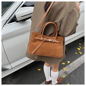 Brown suede baguette bag featuring buckle strap and detachable shoulder strap on street