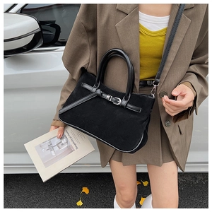 Detail of black suede baguette bag with buckle strap and dual handles in outdoor street view