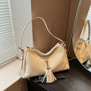 Detailansicht der beigen Cord-Schultertasche mit elegantem Doppelquasten-Metallanhänger