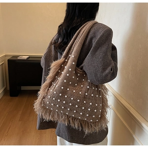 Detail of a brown knitted tote bag featuring pearl embellishments and long feather tassels