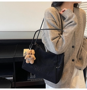 Detailansicht der schwarzen Tote-Bag mit Logo-Prägung und niedlichem Plüschbären-Anhänger