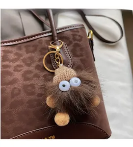 Detail shot of a brown monster plush charm with a knit hat on a leopard print handbag