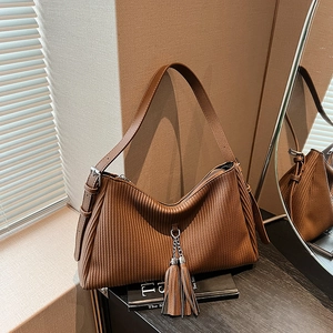 Detail der braunen Cord-Tasche mit Lederfalten und dekorativem Fransenanhänger
