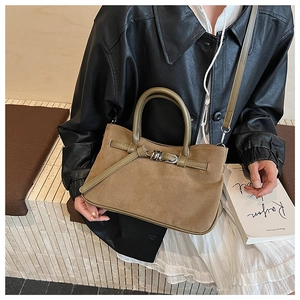 Detail of tan suede baguette bag with buckle knot design held by model in casual outfit