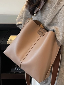 Sac seau en cuir marron avec large bandoulière, porté à l'épaule pour un style chic