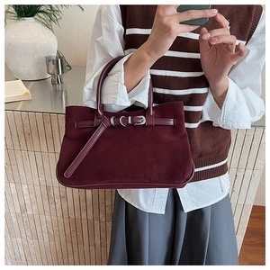 Detail shot of a burgundy suede baguette bag with a stylish metal buckle and leather handle