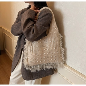 Detailed macro view of beige knitted tote bag with pearls and stylish long fringe trim
