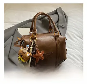 Detail view of brown Boston bag with leather grain, dual handles, and plush bear charm
