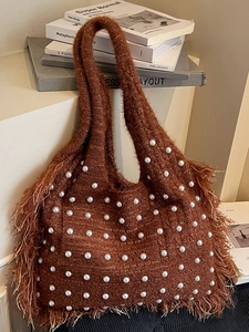 Handmade brown knit tote bag with white pearls and long tassels leaning on books