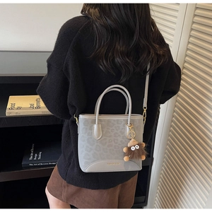 Detail of grey leopard print tote bag with plush monster charm and leather shoulder strap