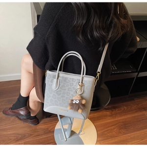 Detail of light grey leopard embossed bucket bag with plush charm and gold logo