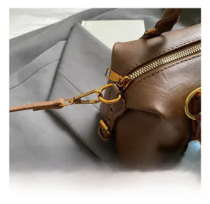 Detailed close-up of golden metal hooks and hardware on a coffee leather Boston bag