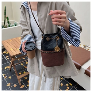 Detail of quilted bucket bag with chain strap and gold pendant in autumn setting