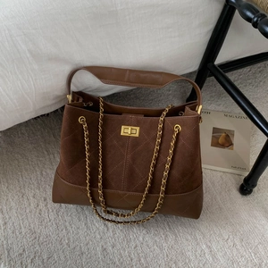 Detail of a brown quilted bucket bag featuring a gold twist lock and a sleek chain strap
