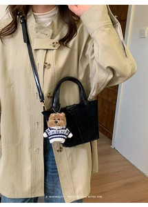 Detail of black suede bucket bag featuring a cute brown bear charm and gold hardware