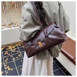 Detail view of large dark brown leather shoulder bag with golden lock in autumn setting