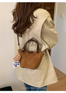 Detail of a brown suede bucket bag with leather handles and a plush bear charm on a model