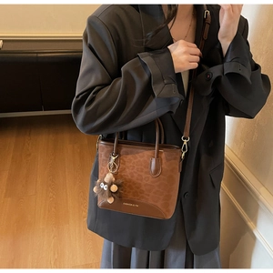Detail view of brown leopard print handbag with plush monster charm and leather strap