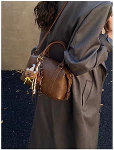 Detail of dark brown Boston bag with teddy bear charm shown on a wool coat