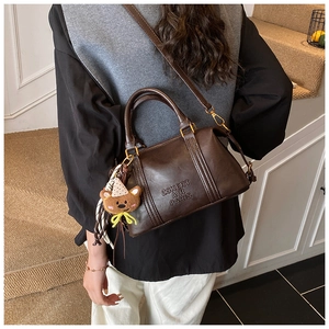 Side view of dark brown leather Boston bag with embossed logo and plush bear charm