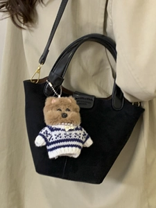 Brown plush puppy bag charm in striped blue sweater hanging on a black leather handbag