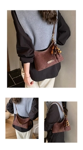 Detail shot of a brown suede shoulder bag featuring bohemian beaded tassels and metal logo