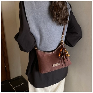 Détail du sac à bandoulière en daim marron avec gland en perles de bois et pièces en bronze