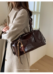 Detail of dark brown wax leather shoulder bag with decorative charms on a beige coat