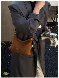 Détail du sac à bandoulière en daim marron avec logo doré et gland sur costume gris