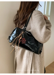 Detail of black glossy shoulder bag with long fringe and leopard bear charm accessory