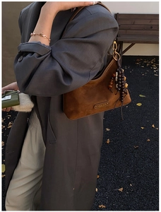 Détail du sac hobo en daim marron avec logo métallique et pompon en perles de bois