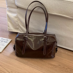 Detail of vintage dark brown glossy leather tote bag on sofa with magazine