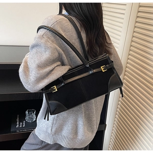 Detail of a vintage black suede baguette bag with gold buckles worn by a model