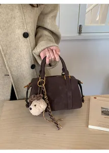 Close-up of vintage brown suede Boston bag with embossed SKERT logo and bear charm