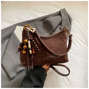 Détail d'un sac cabas en daim marron avec pompon décoratif en perles de bois multicolores