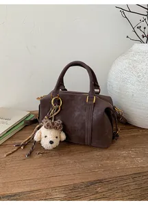 Detail of dark brown suede Boston bag with embossed logo and plush puppy charm