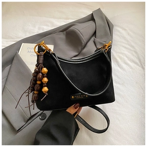 Détail du sac cabas en daim noir avec pampilles en bois posé sur un blazer gris