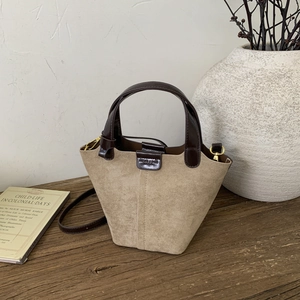 Detail of vintage beige bucket bag with brown handles and gold hardware on a wooden table