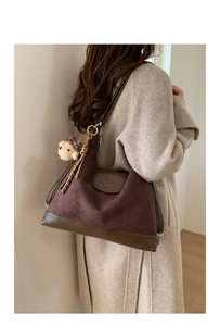 Detail view of deep brown suede tote bag with cartoon engraving and plush bear charm