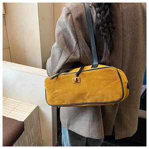 Close-up of mustard yellow suede baguette bag with black leather straps and gold buckle